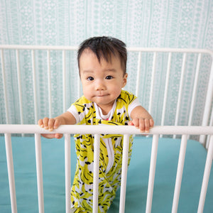 baby in crib, wearing banana print sleep sack with contrasting neon coral zipper. the most giftable baby goods, safe bamboo sleep sack, safe sleep sack