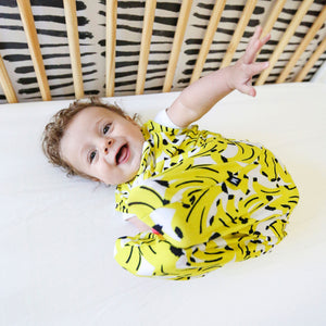 baby in crib, wearing banana print sleep sack with contrasting neon coral zipper. the most giftable baby goods, safe bamboo sleep sack, safe sleep sack