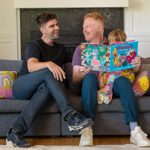 Jesse Tyler Ferguson and Justin Mikita reading to their son Beckett from If You're a Drag Queen and You Know it in MiliMili Modern Rainbow sleep sack and toddler pillows