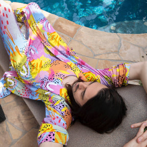 Person lounging by a pool wearing Pronoun by Jesse Tyler Ferguson x MiliMili Modern Rainbow Sleep & Play Romper