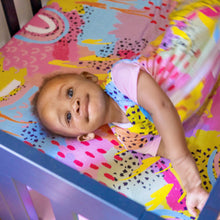 Load image into Gallery viewer, Baby wearing MiliMili x Pronoun by Jesse Tyler Ferguson Modern Rainbow Wearable Blanket on Modern Rainbow Crib Sheet, best crib sheet, bamboo crib sheet
