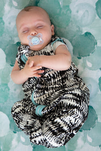 Baby wearing modern black and white sleep sack in the softest bamboo jersey, on top of teal bubbles print bassinet sheet. 