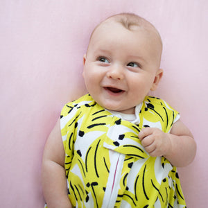 baby in crib, wearing banana print sleep sack with contrasting neon coral zipper. the most giftable baby goods.