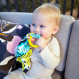 Baby using MiliMili teether for soothing. Tropical palm print lovey with Banana print on reverse side in silky soft bamboo jersey